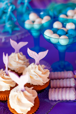 Birthday party concept for girl. Table for kids with cupcakes with withe topind decored purple mermaid tail. Summer season delicious on the party. Sea time theme on the candy bar.の写真素材