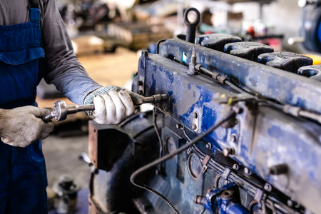 Mechanic repairs old motor of truck in a car repair station. Disassemble engine block vehicle. Motor capital repair. Car service concept.の写真素材