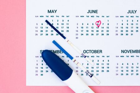 Planning pregnancy. Positive pregnancy tests near calendar page on pink background top view copy spaceの写真素材