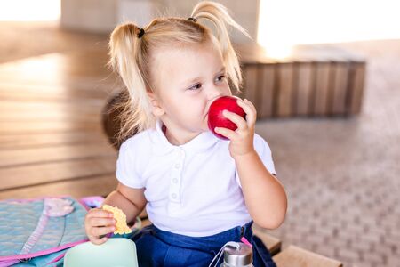 Cute adorable Caucasian toddler baby girl sitting and eating berries fruits. Funny child in park having healthy snack meal. Summer delicious tasty finger food for kidsの写真素材