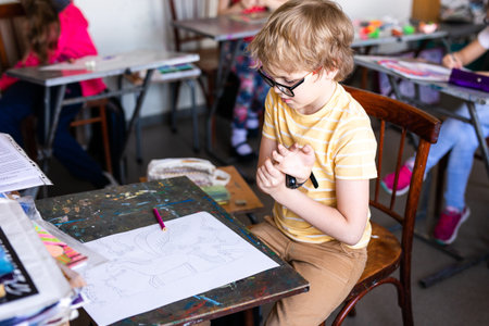 Portrait of cute boy with sketch pen and paper at desk in classroom. Russia, Krasnodar