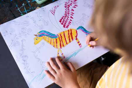 Portrait of cute boy with sketch pen and paper at desk in classroom. Russia, Krasnodar, May, 23, 2019.の写真素材