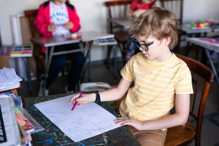 Portrait of cute boy with sketch pen and paper at desk in classroom. Russia, Krasnodar