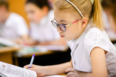 Blonde girl with big glasses sitting in classroom, studing, smiling. Education on elementary school,...