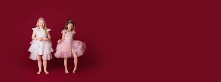 Beautiful little girls princess playing in luxury pink, white and silver dresses isolated on red background. Free space for banner, add, textの写真素材