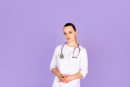 Medical concept of beautiful female doctor in white coat with phonendoscope. Medical student general practitioner. Woman hospital worker looking at camera and smiling, studio, purple backgroundの写真素材