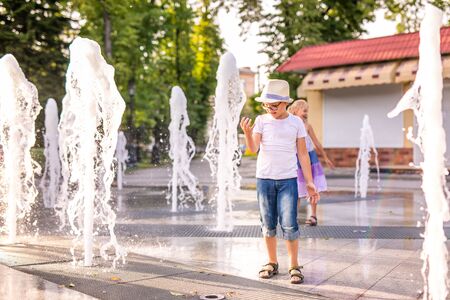 Little caucasian boy in hat playing and having fun with water in fountain in the sunny summer park.の写真素材
