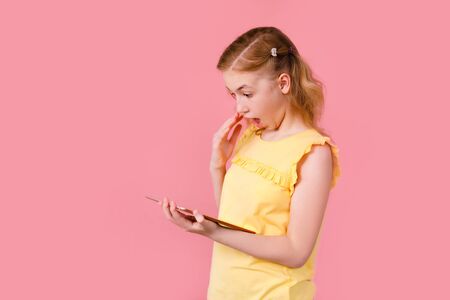 A teenage girl does her homework on a tablet. The student works and communicates with friends. Isolate on a pink background.の写真素材