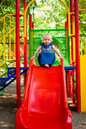 Child playing on outdoor playground. Little baby girl plays on school or kindergarten yard. Active kid on colorful swingの写真素材