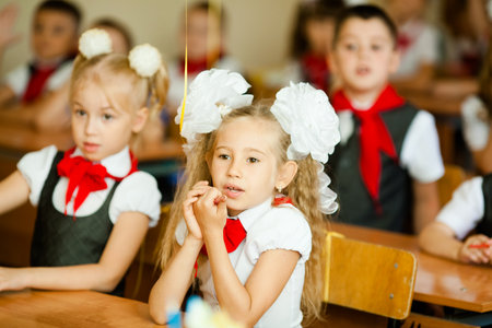 Little first-grader, girl-student goes to school on knowledge day - September First. Student of elementary school in uniform with bows posing in classroom for student Desk, bag with textbooks. Russia, Krasnodar, September, 1, 2017.のeditorial素材