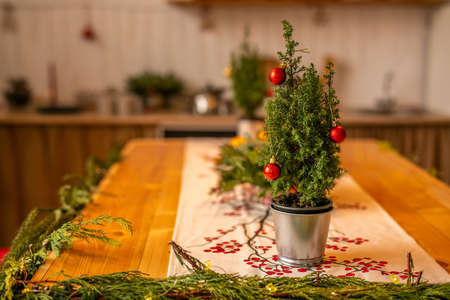 A small Christmas tree with red balls in a metal bucket stands on a wooden table in the decorated kitchen.の写真素材