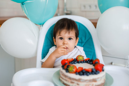Adorable baby boy celebrating first birthday and eating first cake. Kids birthday party decorated with balloons. Child eating cake.の写真素材