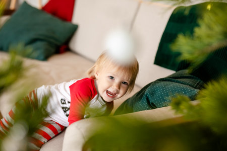 Happy baby girl in red and white pajamas with Christmas gifts near a Christmas tree at home.の写真素材