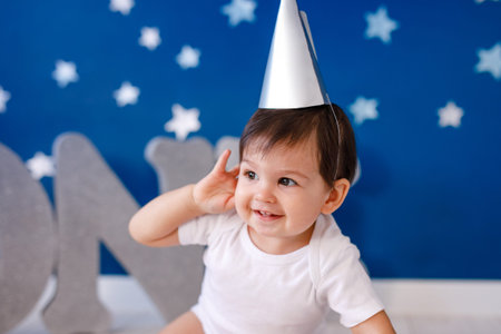 One year old baby boy in white t-shirt celebrates birthday near silver letters ONE on blue...