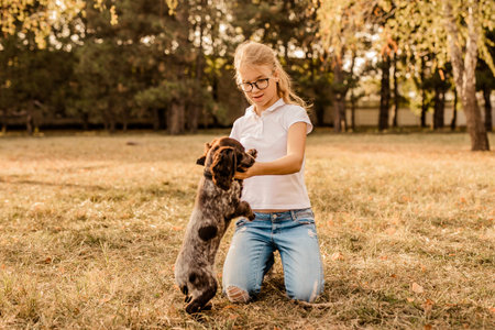Teenager blonde girl with big glasses laughing and playing with little puppy spaniel in the warm...
