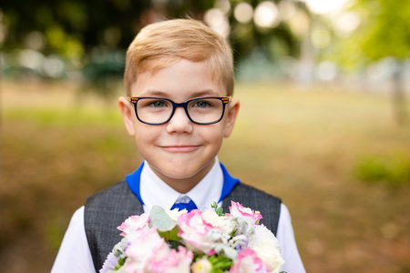 Portrait of a schoolboy with big black glasses and blue tie with flowers for teacher. School backyard, beginning of classes.の写真素材