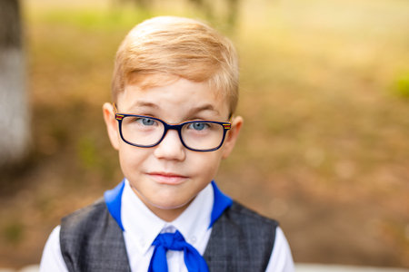Educational theme: portrait of a schoolboy with big black glasses and blue tie. School backyard,...