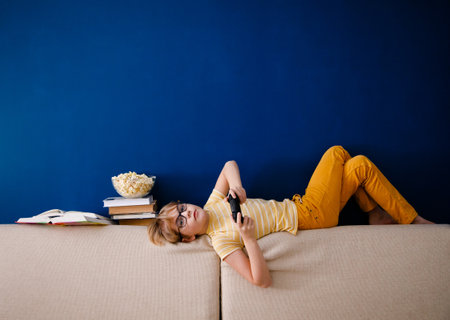 Blonde schoolboy boy plays video games, holds a gamepad, eats popcorn instead of learning lessons on blue background.の写真素材