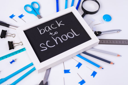 Back to school background with white frame, colorful pencils, square ruler, scissors, clips on pastel blue backdrop. Flat lay, top view, copy spaceの写真素材
