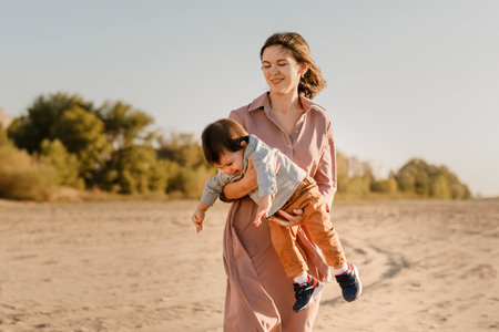 Portrait of happy loving mother hugging her baby son in the sunny park near river.の写真素材