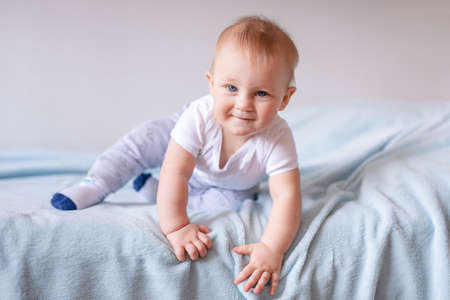 Adorable baby boy in white sunny bedroom. Newborn child relaxing on a blue bed. Nursery for young children. Newborn kid during tummy time with toys at a window.の写真素材