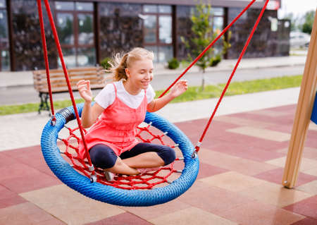 White-haired girl 10 years old playing, swings and slides on the playground in the summer in the city.の写真素材