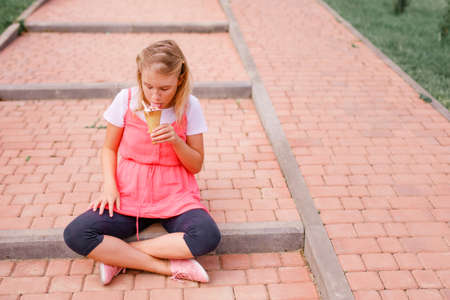 A girl in a pink dress eating a big ice cream in the square.の写真素材
