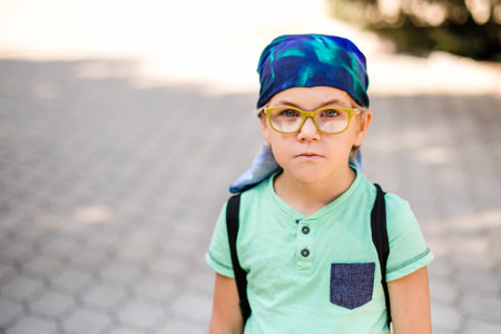 A funny little boy in glasses and a bandana, wearing a green t-shirt and denim shorts, having fun and joking.の写真素材