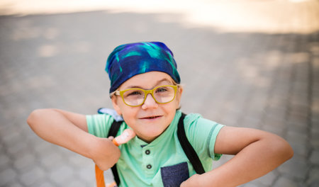 A playful small boy in glasses and a headband, dressed in a green shirt and jean shorts, laughing.の写真素材