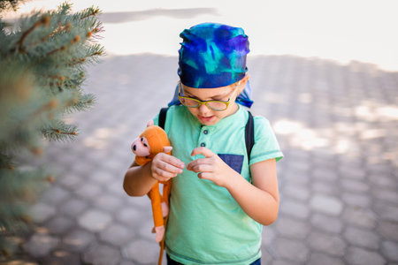 A cute little boy in glasses and a bandana, wearing a green t-shirt, carefully studies a plant while holding a toy monkey.の写真素材