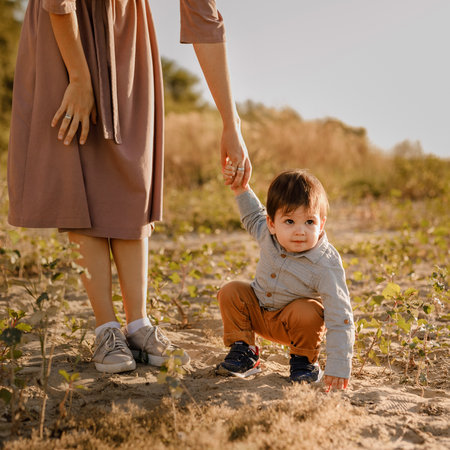 Mom holds her one-year-old baby by the hand for a walk in the park by the river.の写真素材