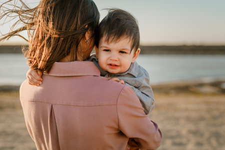 Portrait of happy loving mother hugging her baby son in the sunny park near river.の写真素材