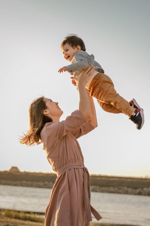 Portrait of happy loving mother hugging her baby son in the sunny park near river.