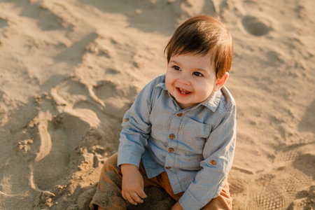 One-year-old boy sitting in the sand, smiling and playing.