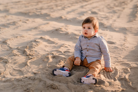 One-year-old boy sitting in the sand, smiling and playing.