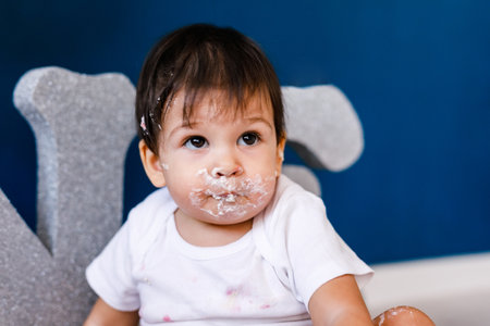 Curious baby boy poking finger in his first birthday cake on blue backgroundの写真素材