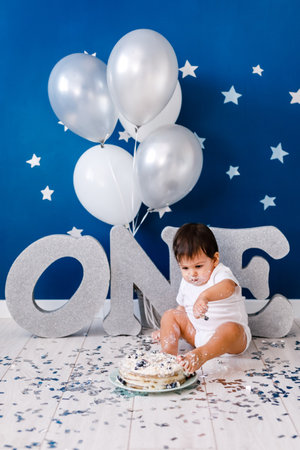 Curious baby boy poking finger in his first birthday cake on blue backgroundの写真素材