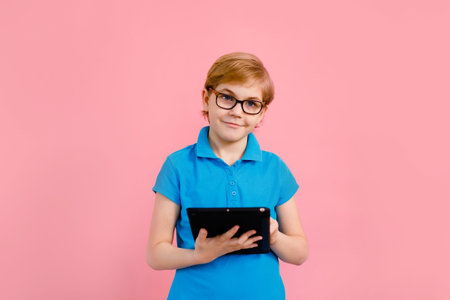 Boy wearing glasses using a tablet on a pink background.