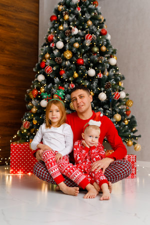 The father embraces his young son and daughter next to the Christmas tree.の写真素材