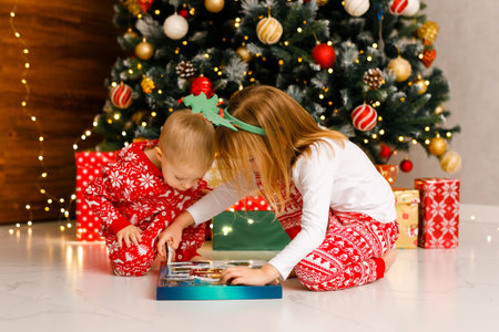 Brother and sister in cozy pajamas are curiously looking at a Christmas giftの写真素材