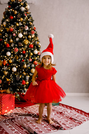 A young girl in a red dress is happily bouncing by the Christmas tree.の写真素材
