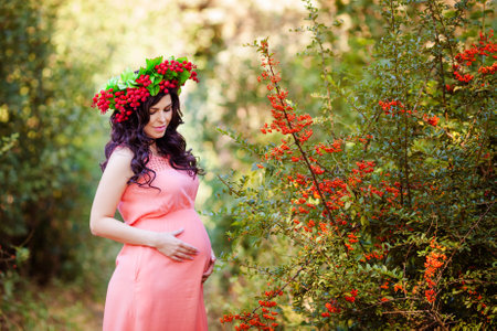 Portret of pregnant women in pink dress with wreath in her head in the warm parkの写真素材