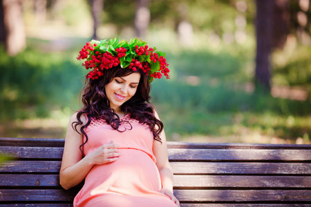 Portret of pregnant women in pink dress with wreath in her head in the warm parkの写真素材