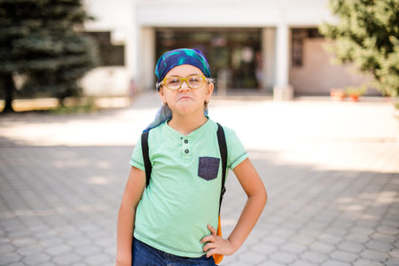 A playful small boy in glasses and a headband, dressed in a green shirt and jean shorts, laughing.