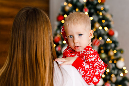 Toddler in festive pajamas is peeking over his mom's shoulder.