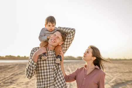 Happy family walking on the road in the park. Father, mother holding baby son on hands and going...
