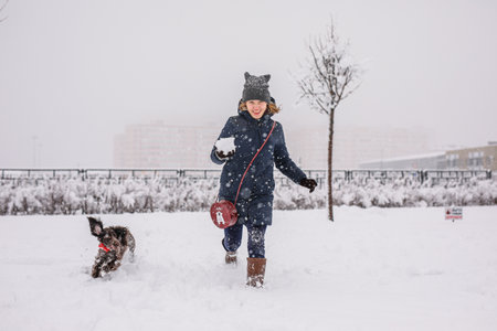 A teenage girl walking her dog outside in winter. Russian spaniel runs with flapping ears in the snow and plays.の写真素材