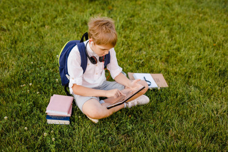 Little school boy studying outdoors school yard on warm sunny day. Student of primary school doing homework. Innovation education for preschool, kindergarten kidsの写真素材
