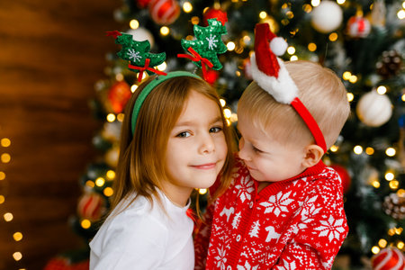 Little brother and sister in red pajamas are standing next to a Christmas tree.の写真素材