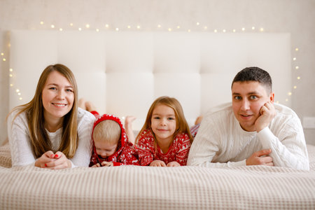 A boy and a girl are lying between their parents on the bed, smiling and embracing the Christmas spiritの写真素材